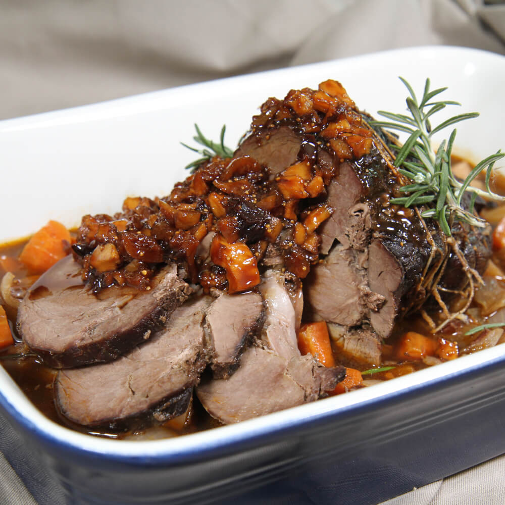 Rezept für Wildschweinkeule mit Dörrobstsoße Wildschweinkeule mit Dörrobst, einer dunklen Soße und frischem Rosmarin in einer blauen Auflaufform serviert