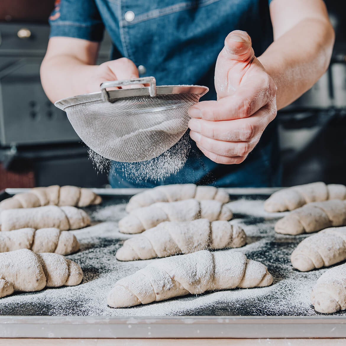 Köstliche Hörnchen Frisch gebackene Hörnchen, leicht mit Puderzucker bestäubt - goldbraun und knusprig auf einer Backfolie.