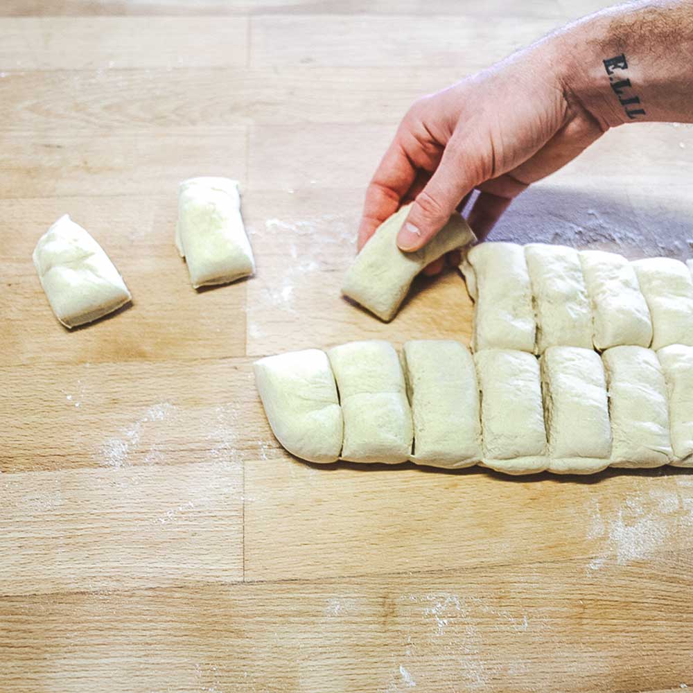 Teigteiler eckig Eine Person entnimmt die einzelnen Teiglinge, die mit dem Abstechwerkzeug abgestochen wurden, auf einer Küchenarbeitsplatte.