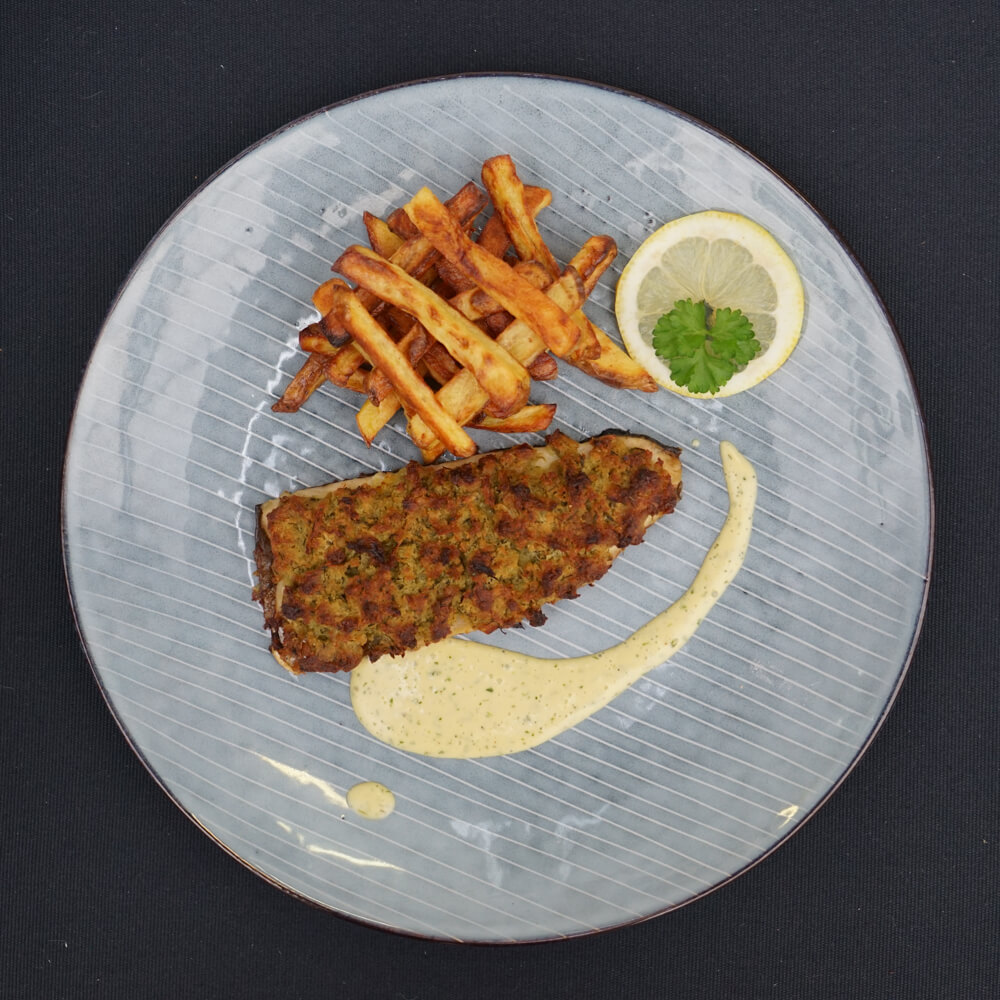 Rezept für Saibling à la Bordelaise mit Ofenpommes & glasierte Möhren Saibling à la Bordelaise Ofenpommes, einer Bärlauch Hollandaise und einer Scheibe Zitrone und etwas Petersilie auf einem hellblauen Teller angerichtet