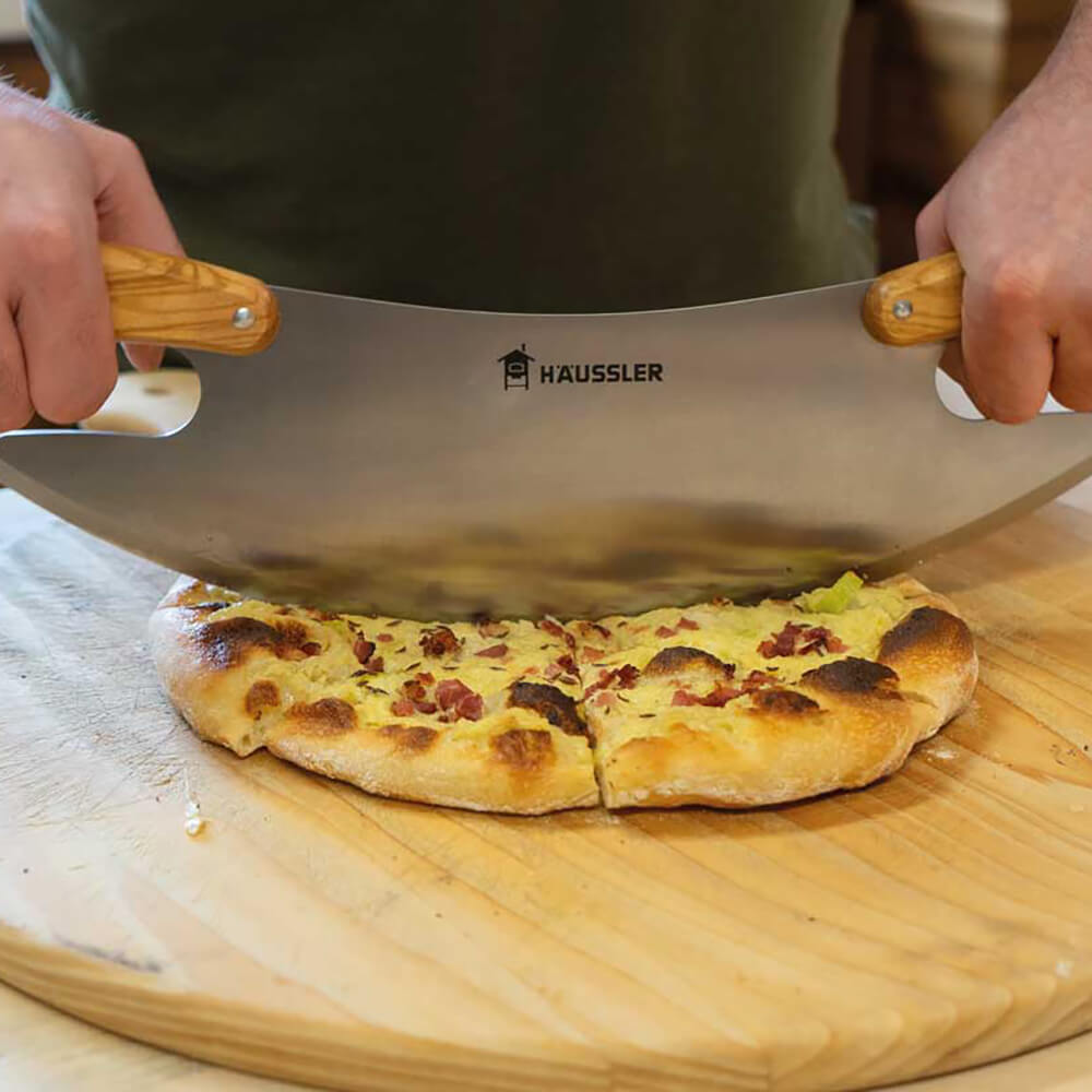 Pizza-Wiegemesser in der Anwendung beim Schneiden einer frisch gebackenen Dinnete auf einer Holzplatte.