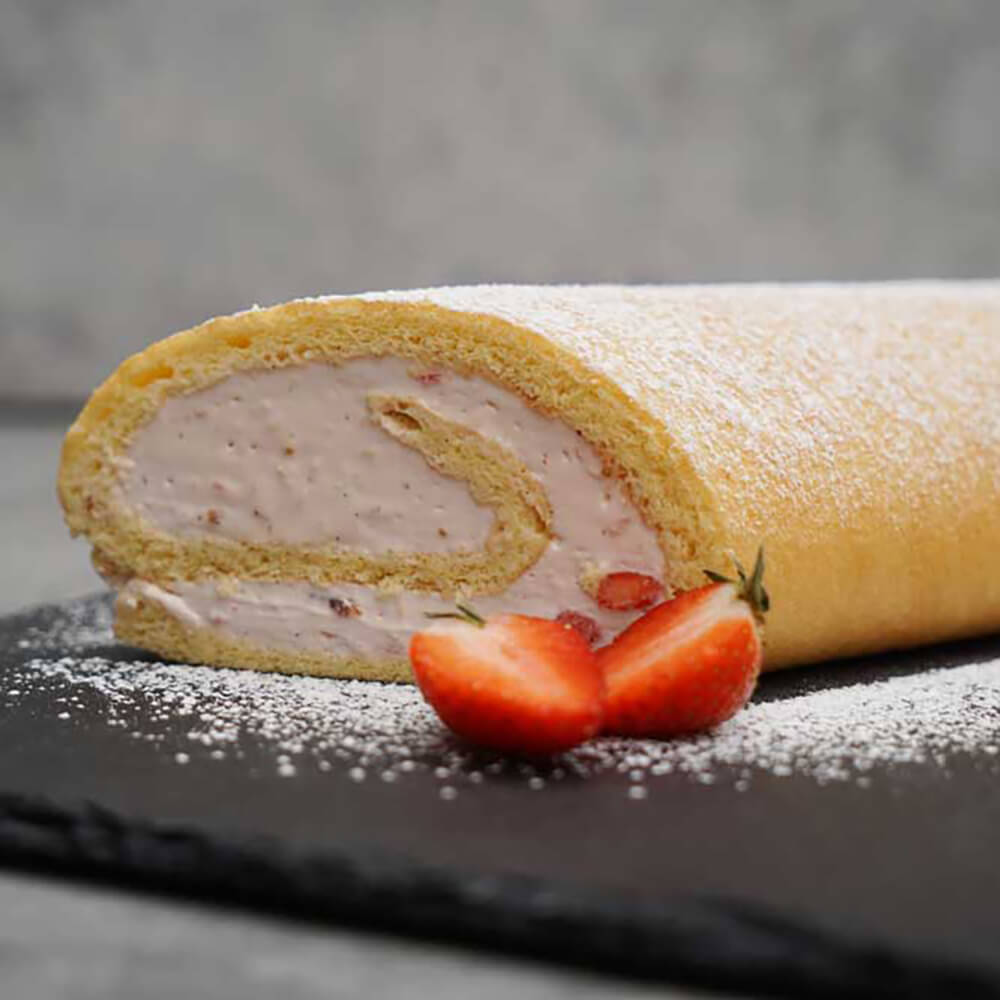 Biskuitroulade auf schwarzer Platte liegend - im Vordergrund liegt eine durchtrennte Erdbeere