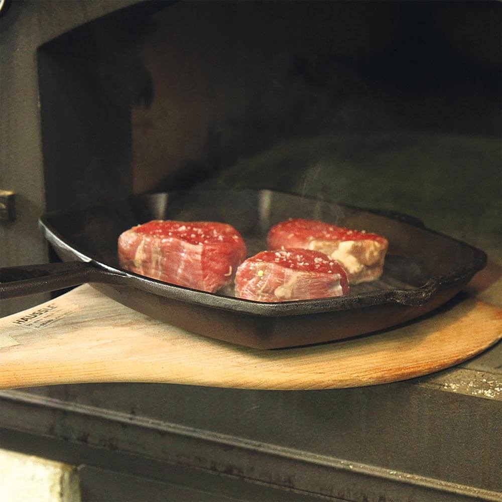 Eisengusspfanne mit Fleisch wird auf einem Backschieber in den Ofen geschoben