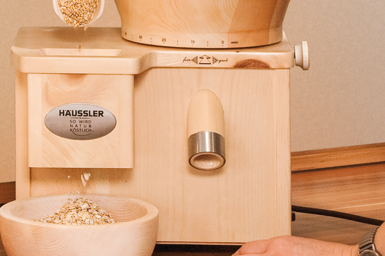 Flockenquetsche Flockenquetsche bei der Verarbeitung von Hafer - frische Flocken fallen in eine Schale.