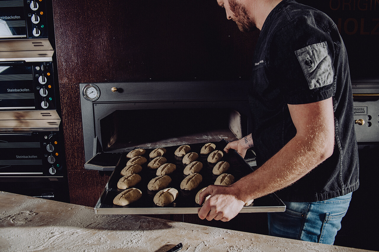 Bäcker schiebt Teiglinge in einen Holzbackofen