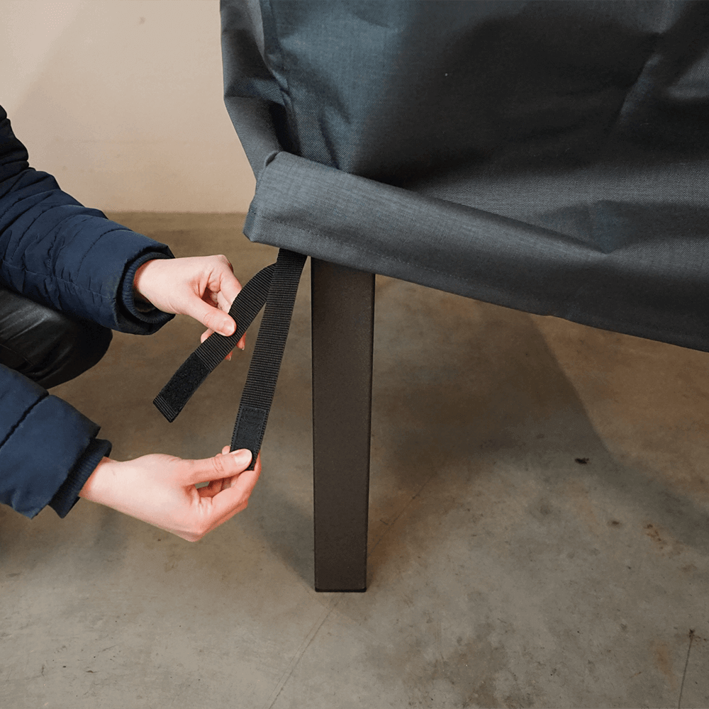 Hände, die die Befestigungslasche einer Holzofenabdeckung halten neben einem Ofenbein