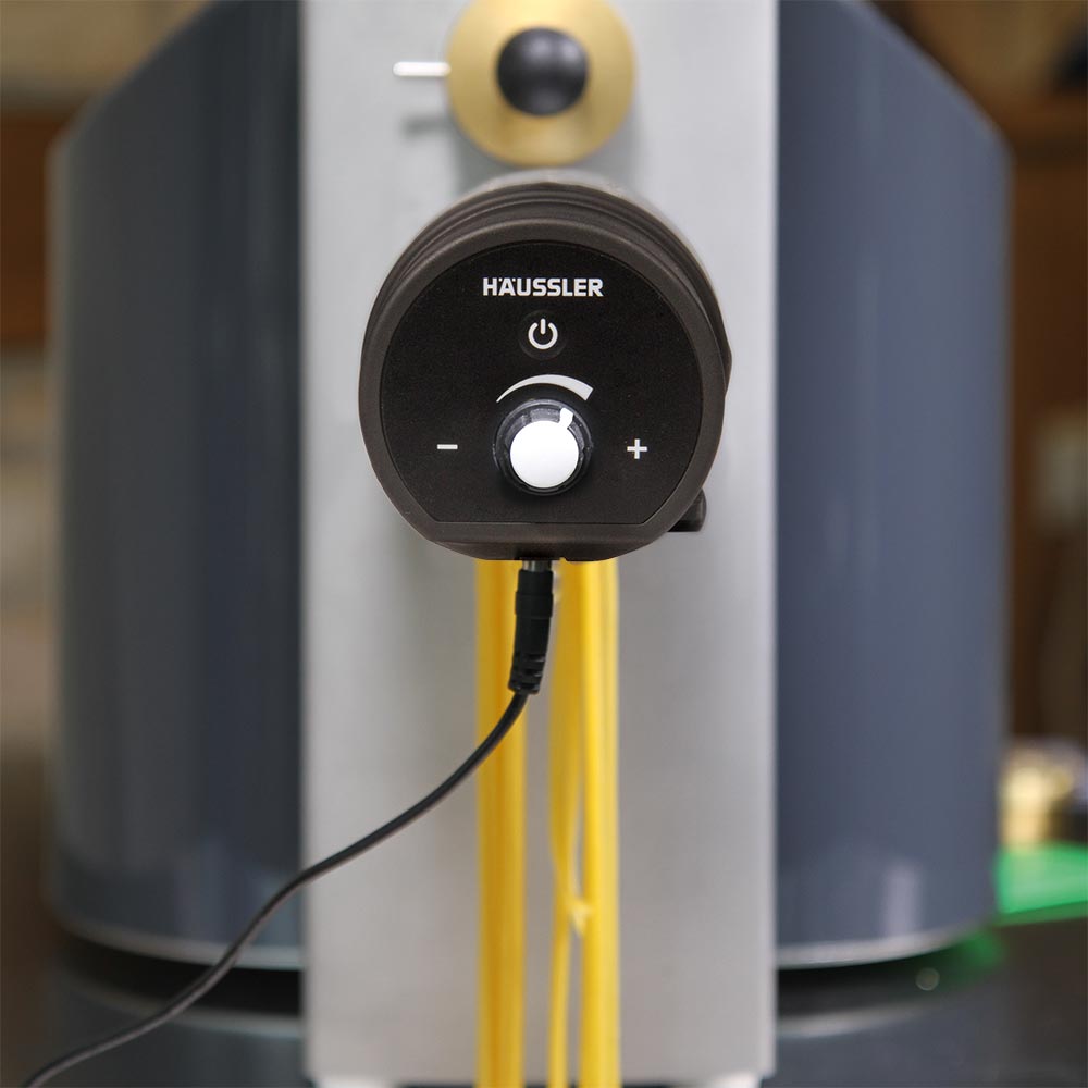 Ein Nudelschneider wird von vorne gezeigt. auf dem schwarzen Kunststoff ist das Häussler Logo abgebildet und ein Drehknopf um die Geschwindigkeit des Messers einzustellen. Zusätzlich befindet sich dort noch der An- und Ausschaltknopf.