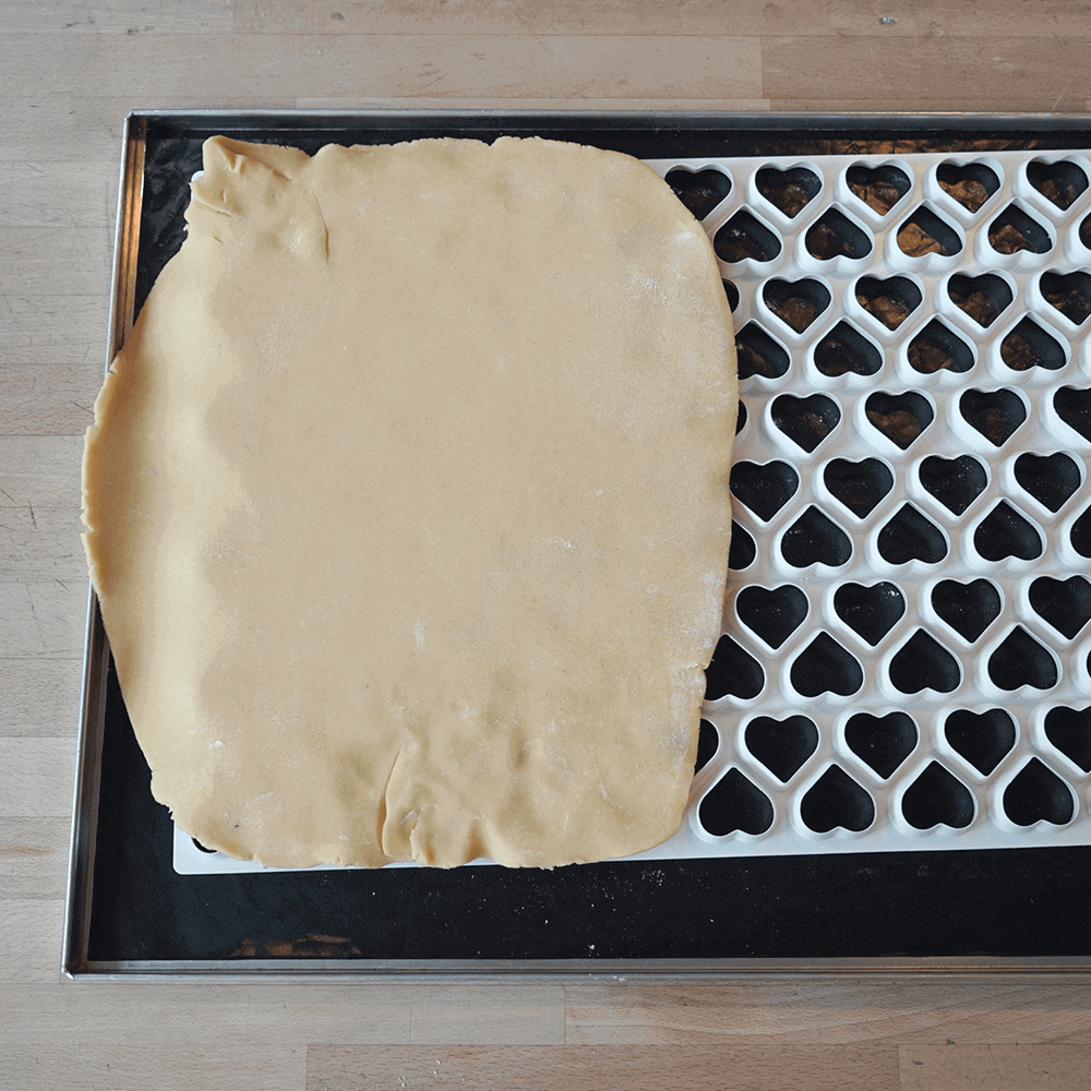 Ausstechmatten für die Plätzchenproduktion Die Ausstechmatte mit dem Muster Herzen wird angewandt. Der Plätzchenteig liegt über der Ausstechmatte