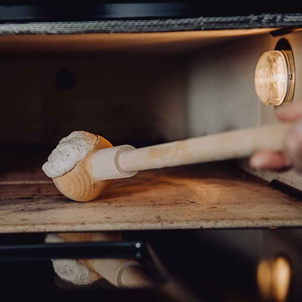 Ein Brötchen wird mit einem Knauzenschießer gerade in einen Elektrosteinbackofen eingeschossen