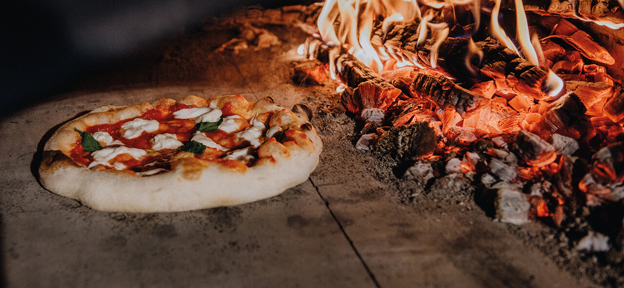 Pizza backt direkt an der Glut in einem traditionellen Holzbackofen - der Boden wird knusprig durch die intensive Hitze.