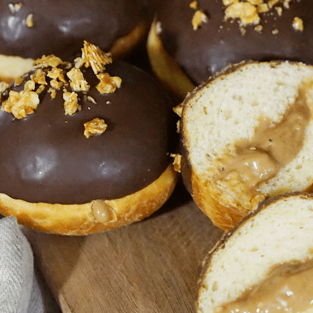Rezept für Krapfen mit Nougatfüllung mehrere Krapfen mit Nougatfüllung, einer Schokoglasur oben drauf und mit Krokant verziert auf einem Holzbrett serviert