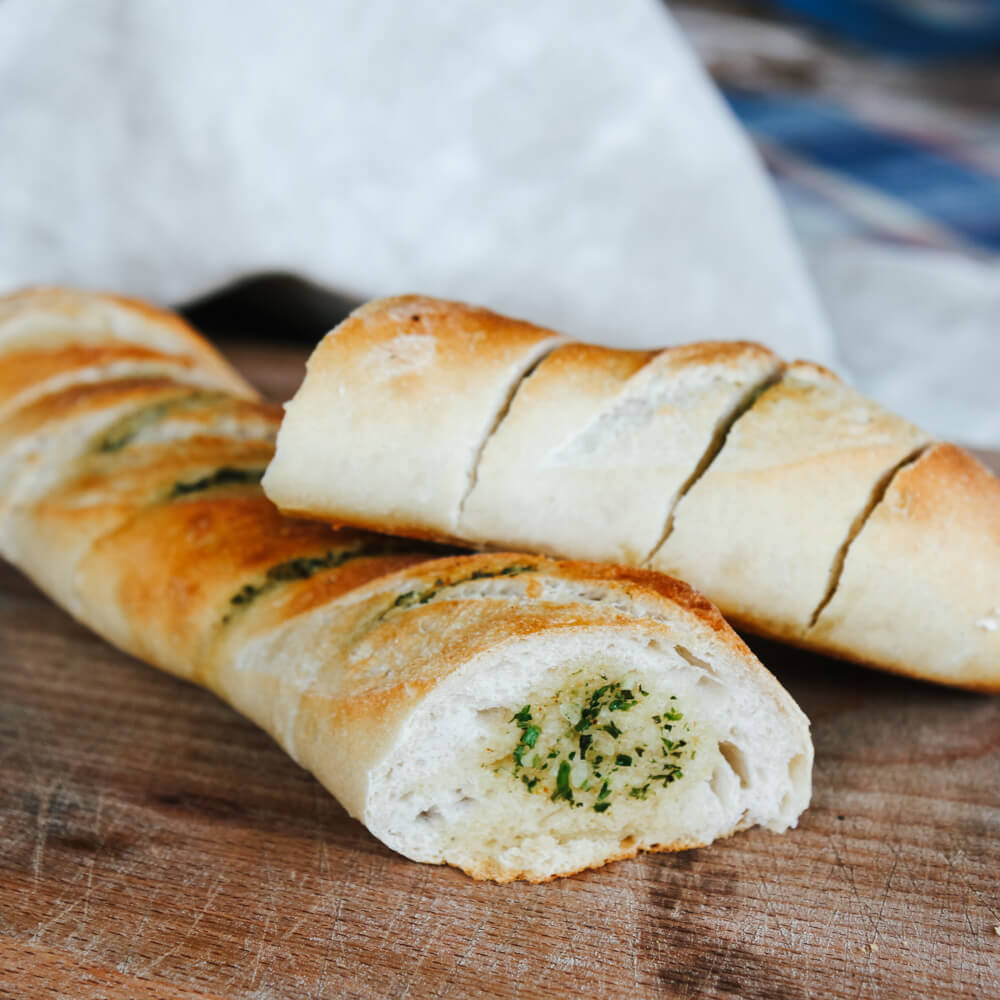 aufgeschnittenes, selbstgemachtes Kräuterbutterbaguette auf Holzbrett