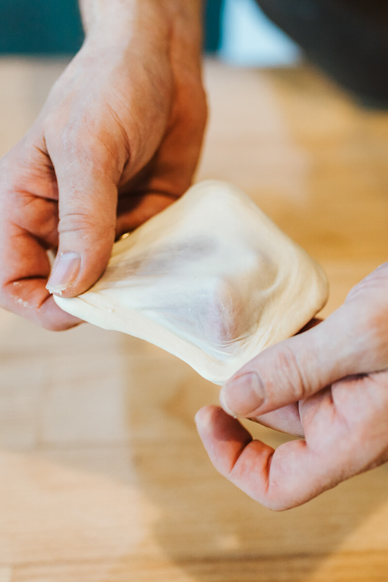 Zwei Hände ziehen einen Teig um zu überprüfen ob der Teig fertig geknetet ist