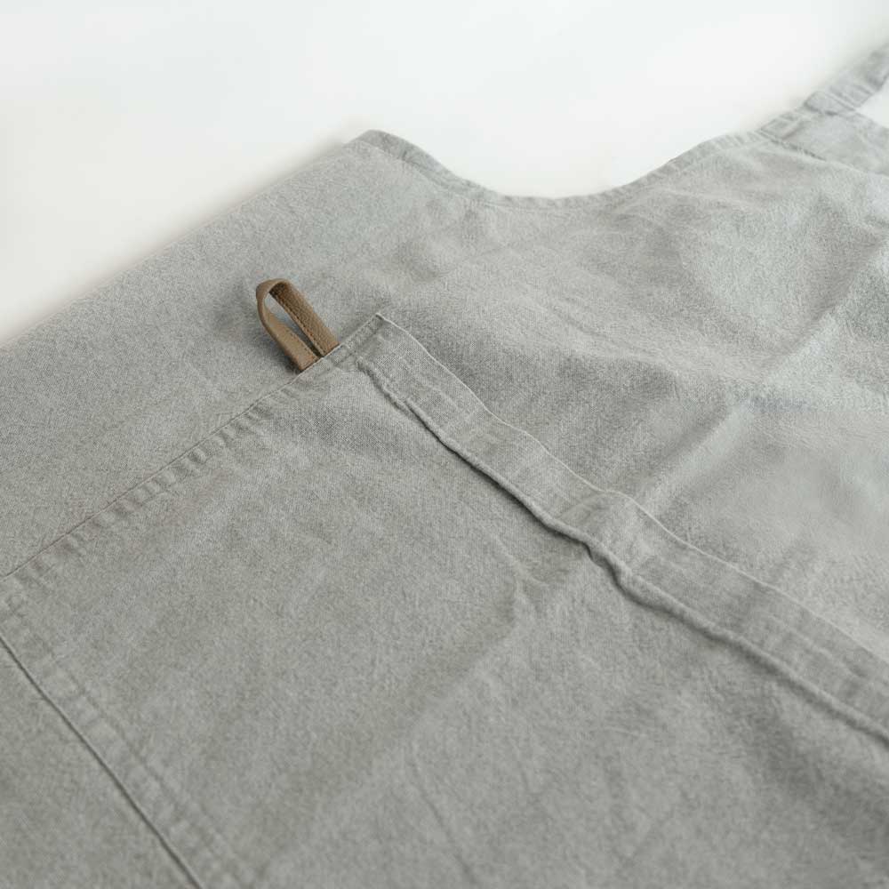 Schürze "MYRNA" grau Auf dem Bild befindet sich ein Ausschnitt einer grauen Schürze auf dem zu erkennen ist, das die schürze eine Tasche besitzt.