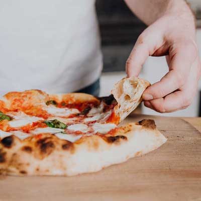 Eine Hand greift ein geschnittenes Stück Pizza
