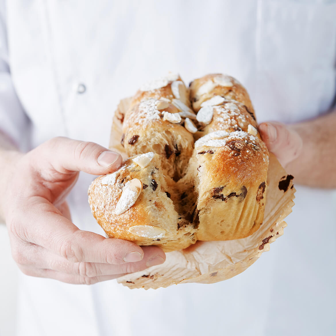 Frisches Brioche Frisches Brioche wird in der Hand gehalten - goldbraune Kruste, weiche, fluffige Textur sichtbar.