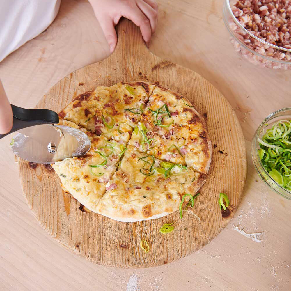 Pizzaschneider schneidet Pizza auf einem hölzernen Servierbrett