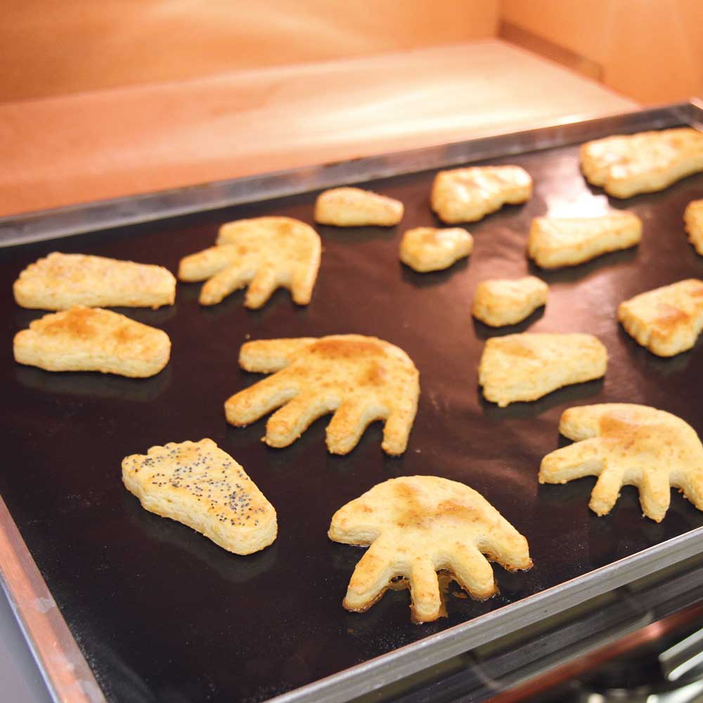 Plätzchen mit Käsefuß-Ausstecher Plätzchen aus Hand- und Fußausstechern auf einem Backblech mit Dauerbackfolie in einem Ofen.