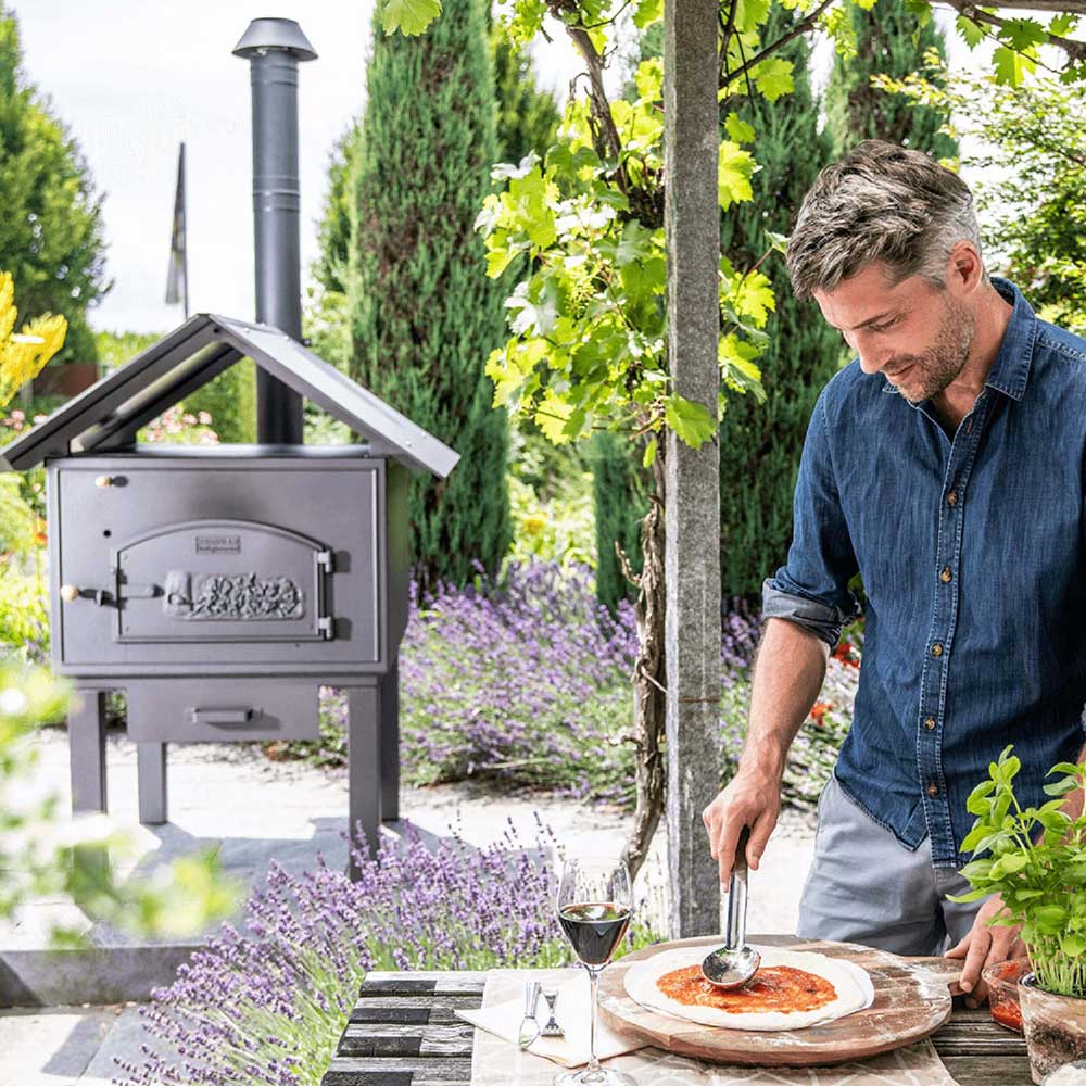 Pizzasugo-Löffel im Einsatz im Garten mit blühendem Lavendel vor einem Holzofen