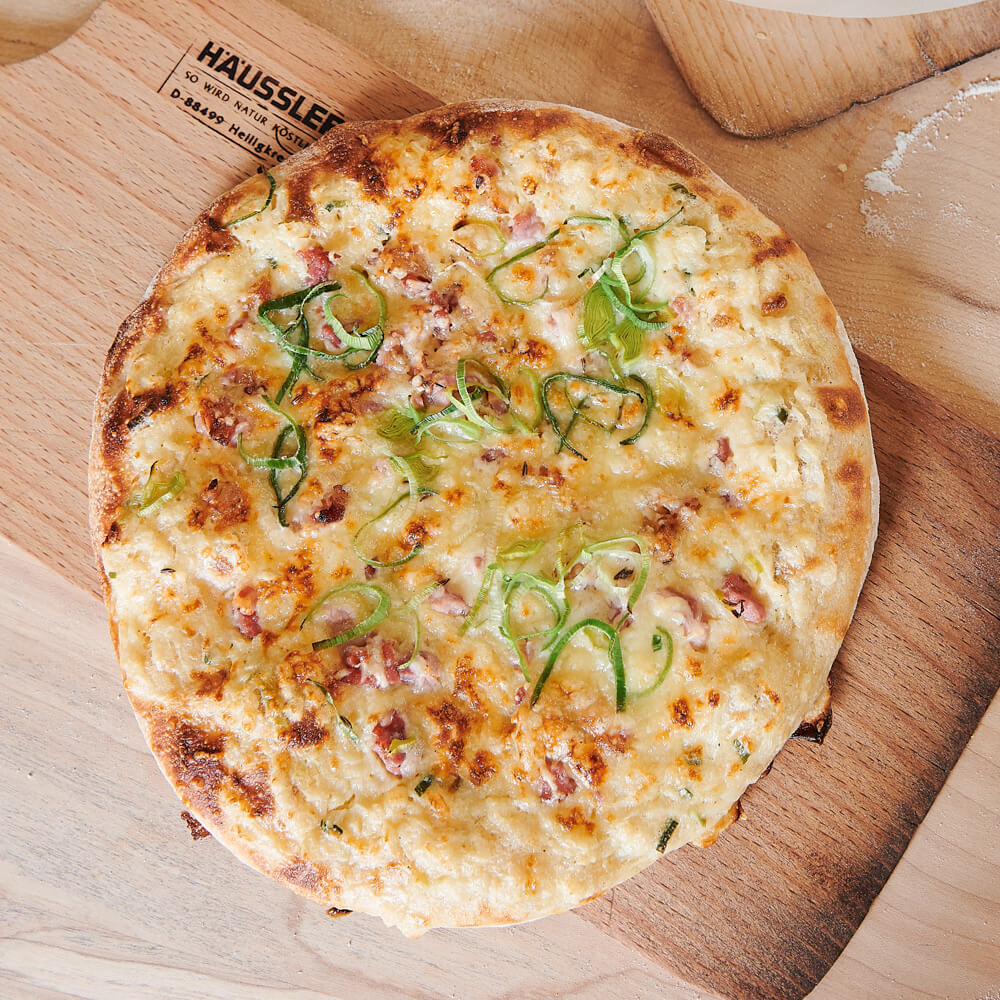 frisch gebackene Dinnete mit Zwiebel, SPeck und Lauchzwiebeln auf einem Backschieber