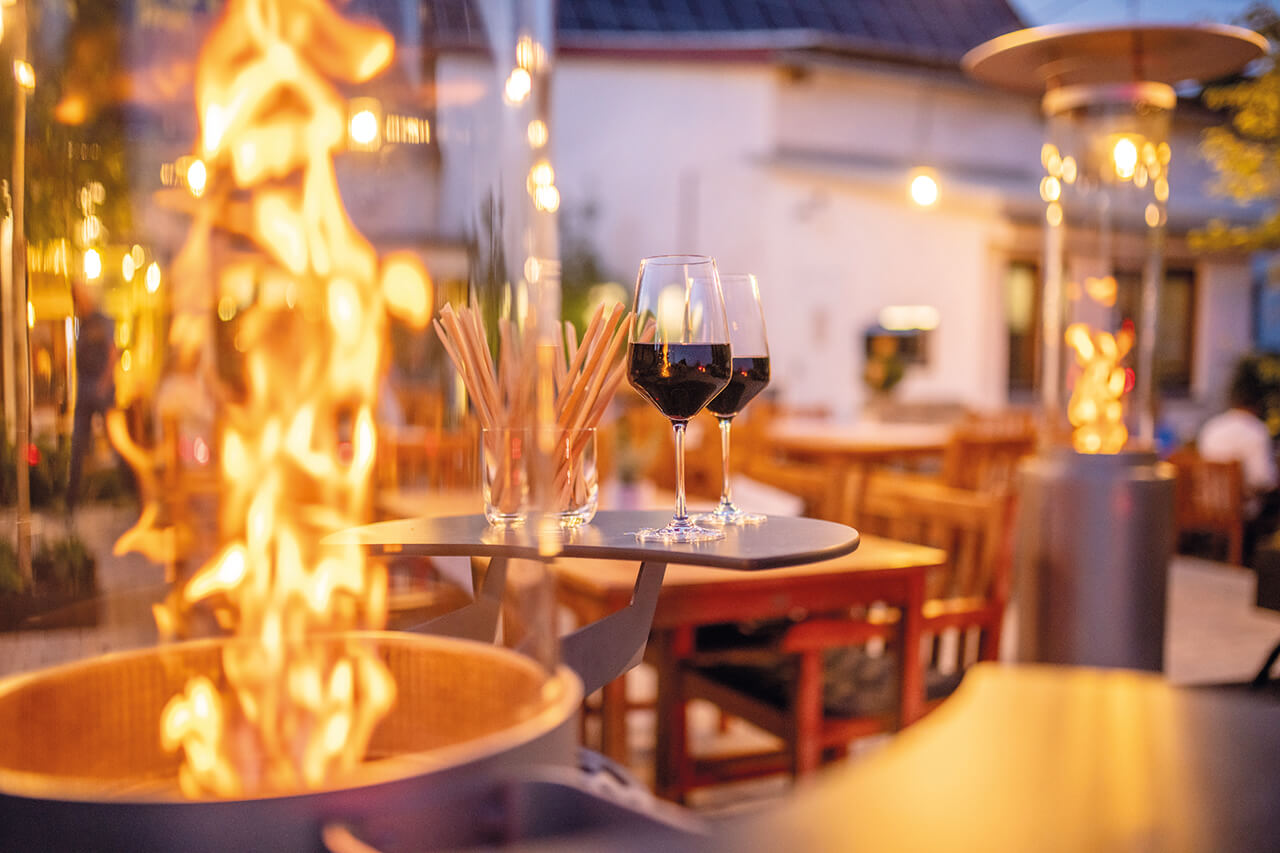 Ambientelicht_auf_Terrasse Warme Lichtstimmung mit Ambientelicht und offenem Feuer - eine gemütliche Atmosphäre bei Abenddämmerung, ideal für entspannte Stunden im Freien.