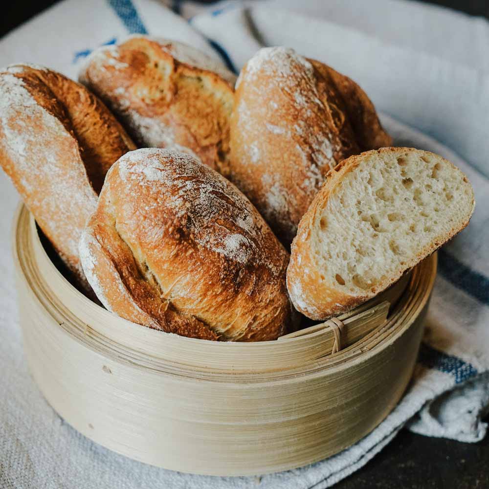 Rezept für Krusti-Semmel Langzeitführung mehrere Krustisemmel in einem Brotkorb auf hellem Tuch