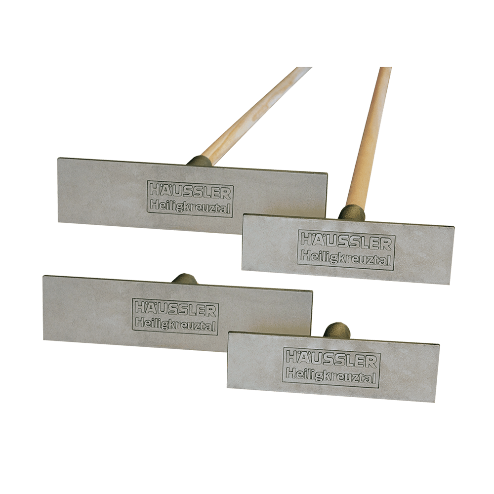 Ascheausziehkrücke Recheckige, aus Aluminiumgussgefertigte Ascheausziehkrücke mit der Prägung "Häussler Heiligkreuztal". Der Stiel ist aus hellem Holz gefertigt. Auf dem Bild sind alle 4 Varianten (zwei Größen, mit und ohne Stiel) zu sehen.