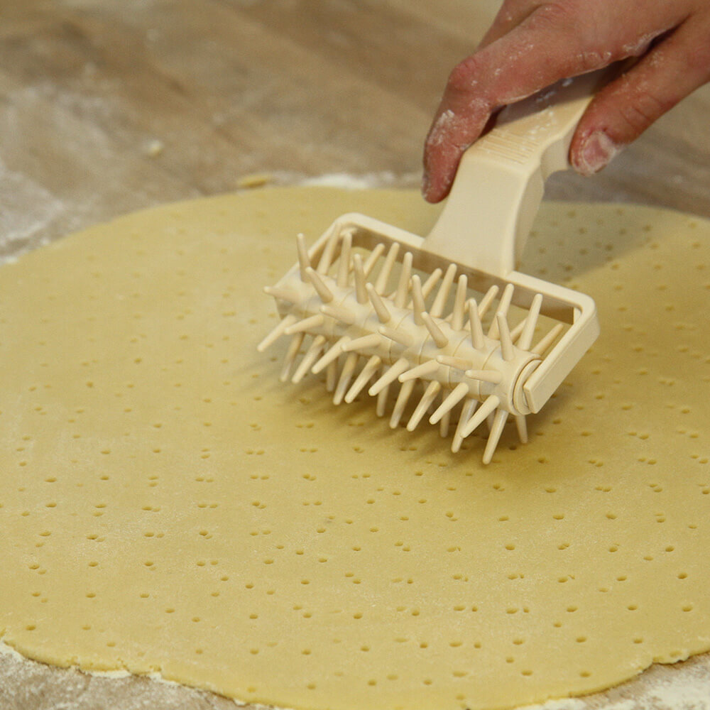 Beigefarbene Rolle mit Griff die über einen ausgerollten Teig fährt