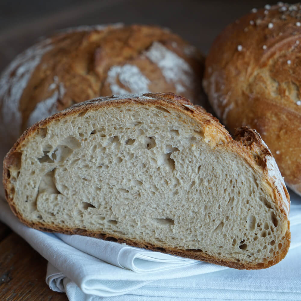 Rezept für Ackerkruste frisch gebackenes Brot leicht mit Mehl bestäubt, in der Mitte halbiert auf einem wei0en Geschirrtuch