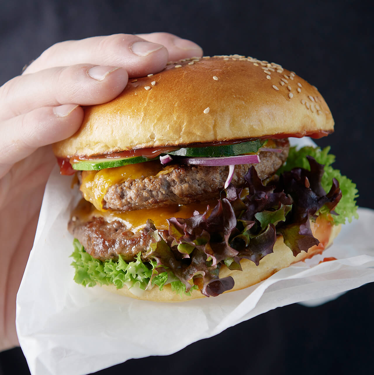 Frisch zubereiteter Burger mit saftigem Fleischpatty, geschmolzenem Käse, Gurken, grünem Salat und einem goldbraunen Burgerbrötchen.