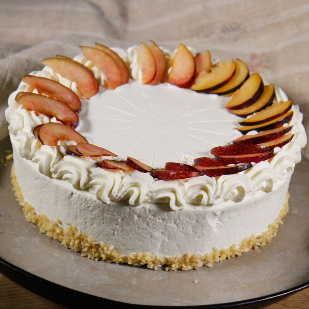 Rezept für Glühwein-Sahnetorte eine Torte eingestrichen mit leicht rosaner Sahne und verziert mit in Scheiben geschnitten Pflaumen auf einer Metall-Kuchenplatte