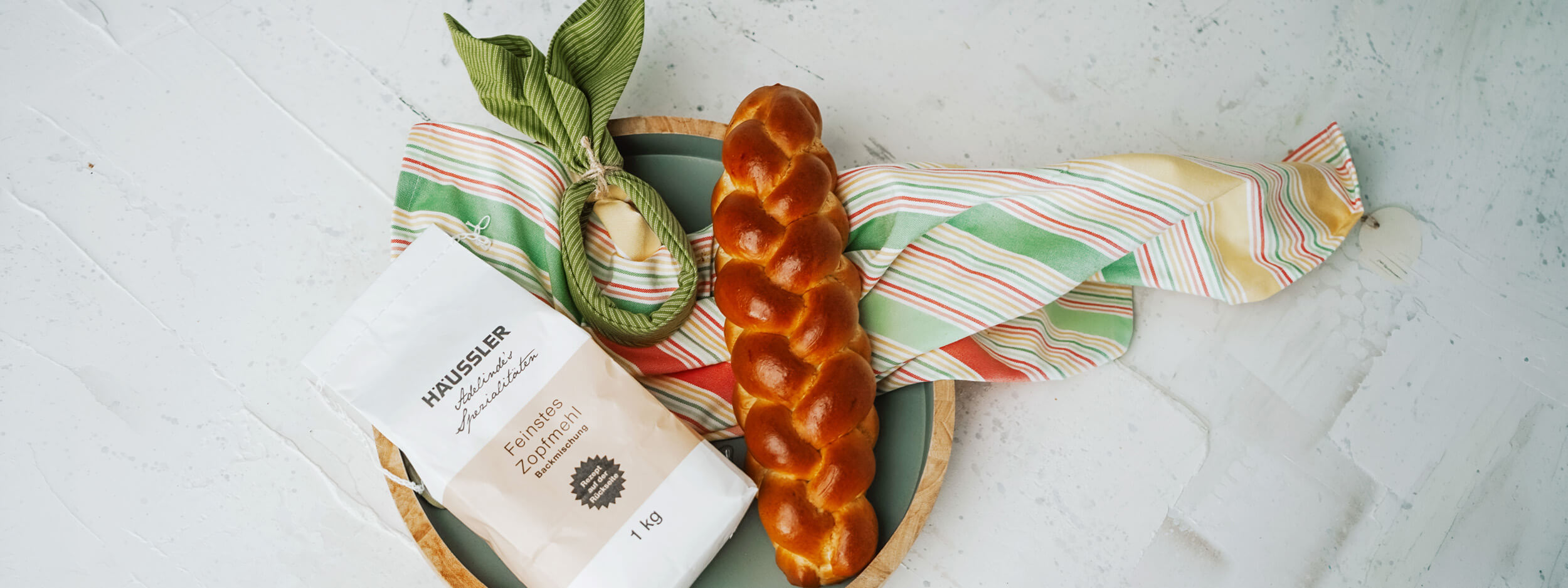Liebevolle Mitbringsel und Geschenke Häussler feinstes Zopfmehl, frisch gebackener Hefezopf liegen im Brotkorb