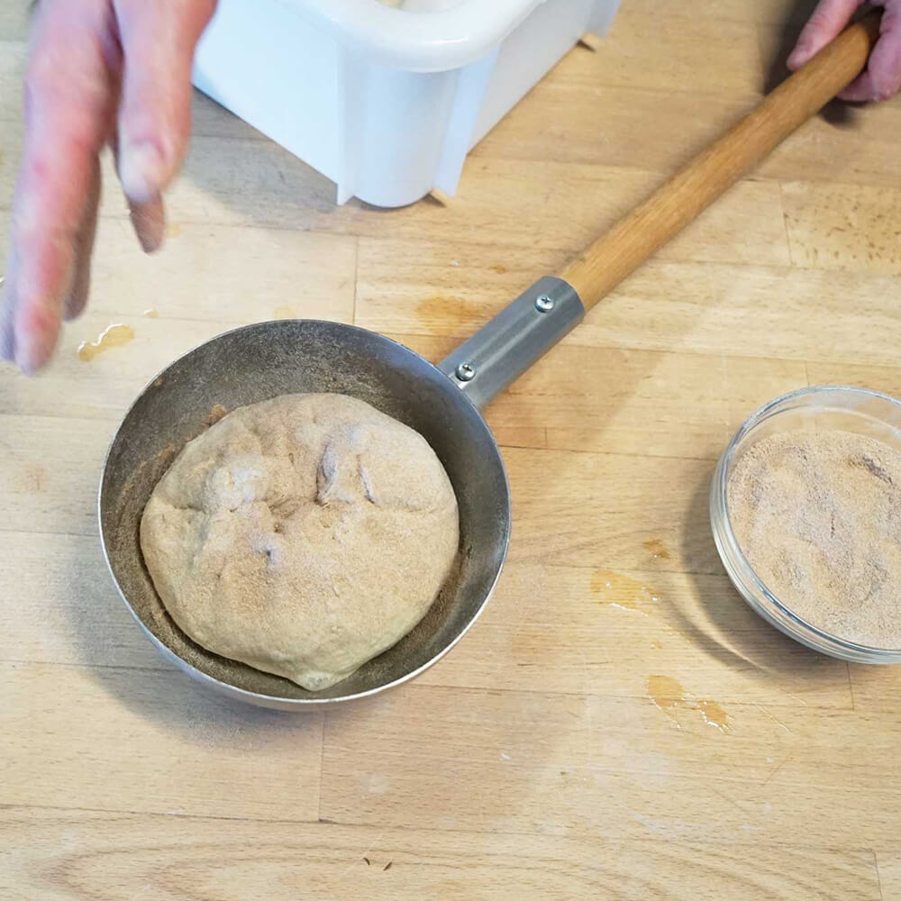 Es wird gerade ein bemehlter Teigling in eine Einnetzschüssel aus Edelstahl gelegt.