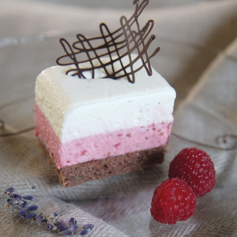 Rezept für Himbeer-Vanille-Panna Cotta gescchichtete Vanille- und Himbeer-Panna Cotta auf einem schokoladen Biskuitboden. Serviert auf einem Glasteller mit ein paar Lavendelblüten und ein paar Himbeeren