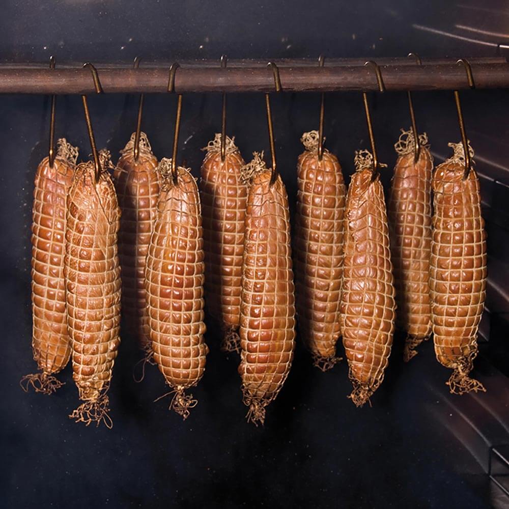 Fleischstücke im Bratenräuchernetz hängen im Räucherschrank