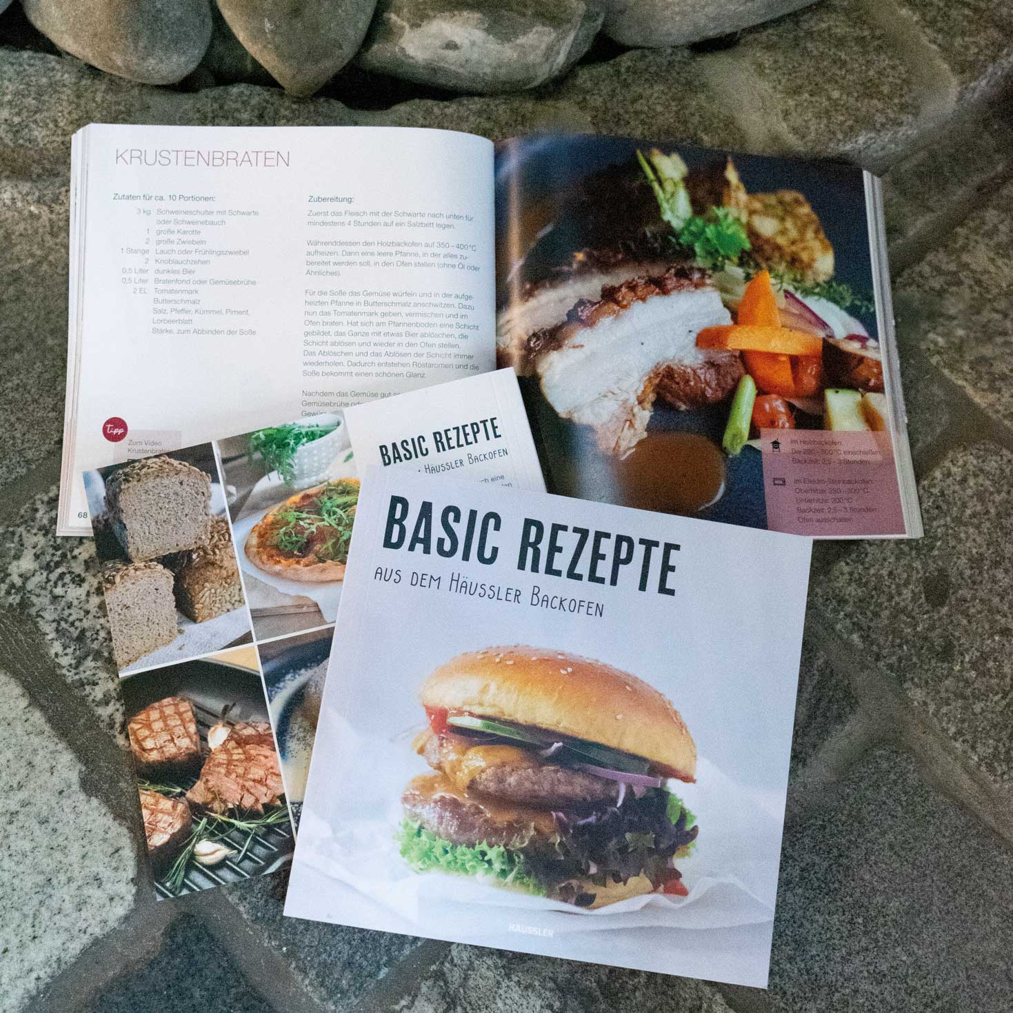 Häussler-Buch: Basic Rezepte aus den Häussler Holzbacköfen Das Häussler Buch: "Basic Rezepte aus dem Häussler Backofen" liegt aufgeschlagen und geschlossen nebeneinander auf einem Pflasteruntergrund