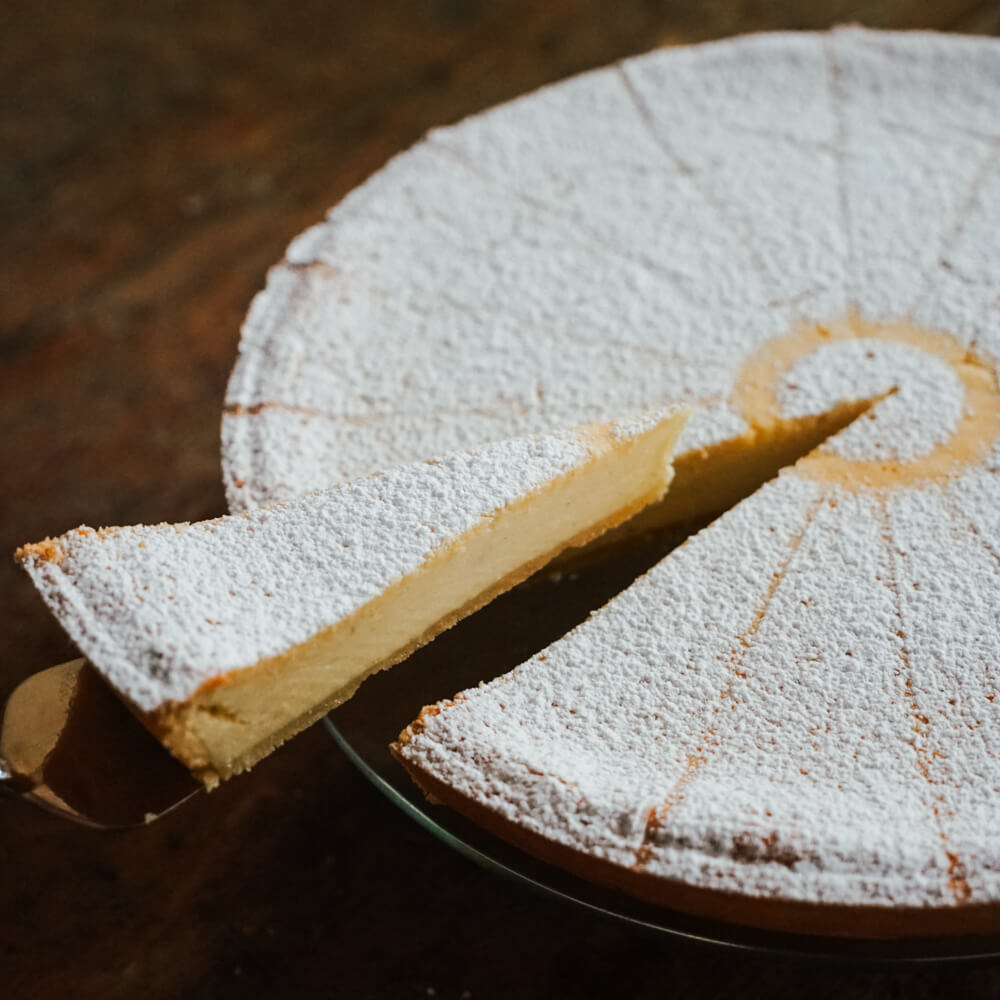 cremiger Käsekuchen mit Puderzucker bestreut aus dem gerade ein Stück herausgehoben wird