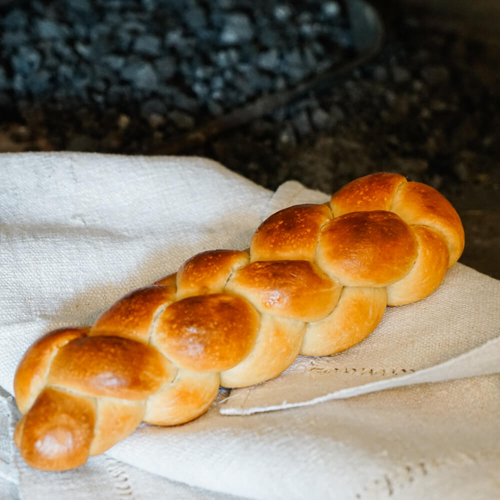 Rezept für Hefezopf frisch gebackener Hefezopf auf hellgrauem Tuch mit einem dunklen Hintergrund