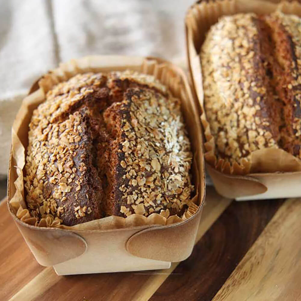 Dinkelvollkornbrot in Holzbackformen auf einem Holzbrett serviert