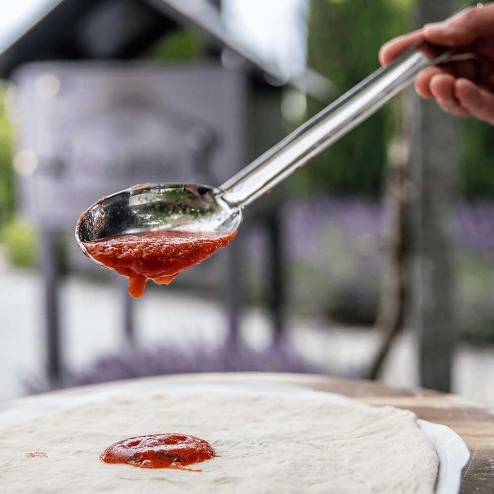 Pizzasugo-Löffel Pizzasugo-Löffel mit Tomatensoße über Pizzaboden