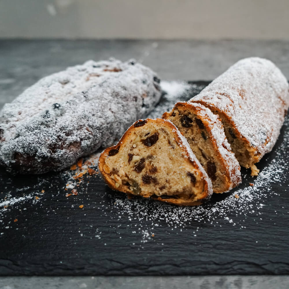 Rezept für klassischen Christstollen Christstollen aufgeschnitten und mit Puderzucker bestreut auf einer Schieferplatte