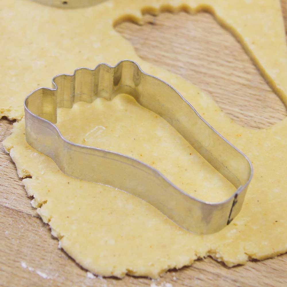 Käsefuß-Ausstecher auf einem ausgerollten Teig auf einer Holzarbeitsplatte.