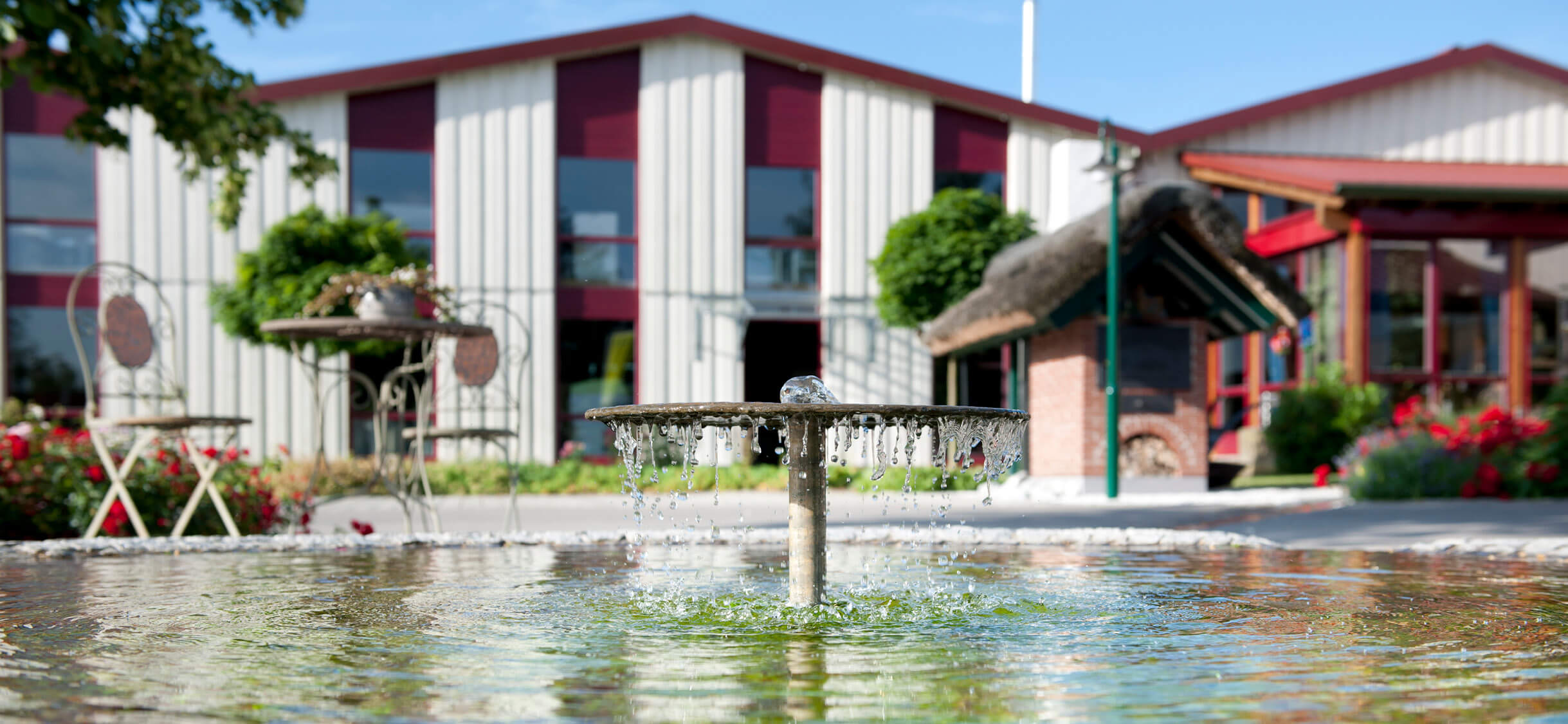 Innenhof des Backdorfs mit einem zentralen Brunnen, umgeben von Backhäusern und Sitzgelegenheiten - eine einladende Atmosphäre im Freien.