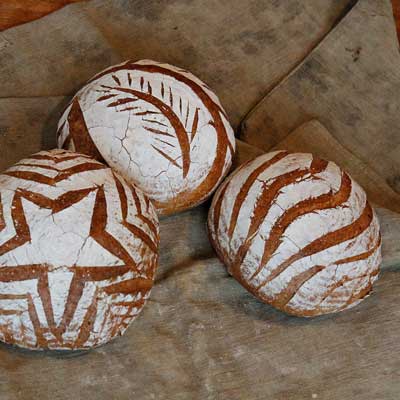 3 Brotlaibe mit unterschiedlichen Mustern an der Oberfläche auf einem braunen Leinentuch liegend