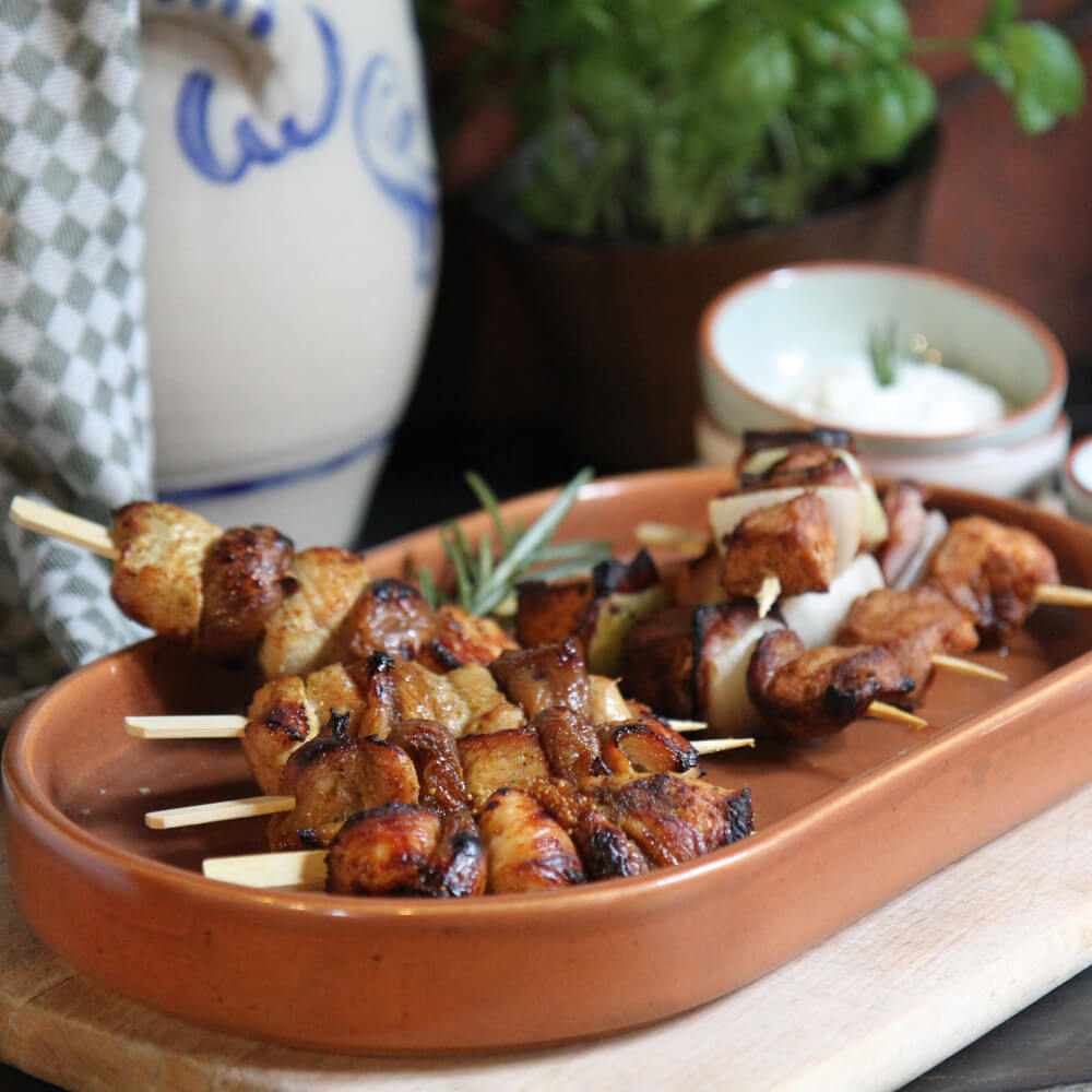 selbstgemachte Grillspieße mit Schweinefleisch, Speck und Zwiebeln in einer brauen Tonschale serviert