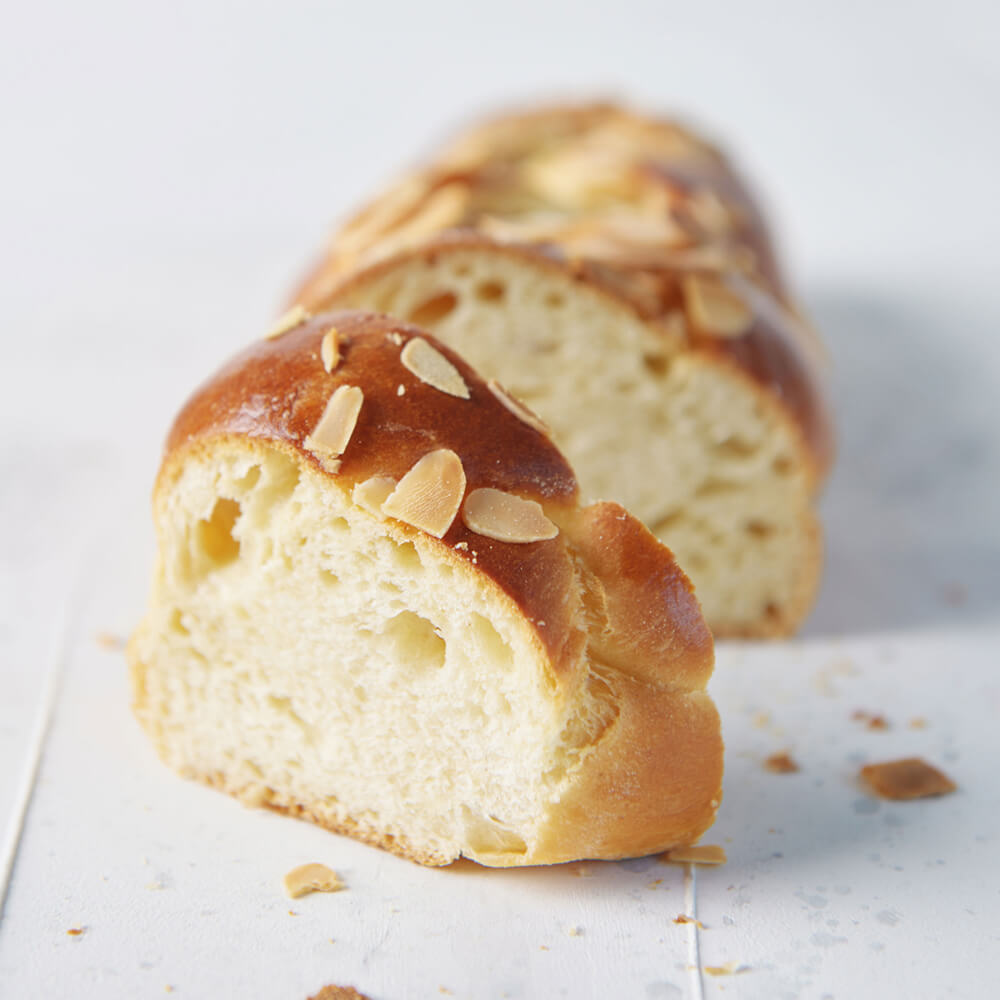 Feinstes Zopfmehl Hefezopf mit Mandelblättchen auf weißem Holzhintergrund