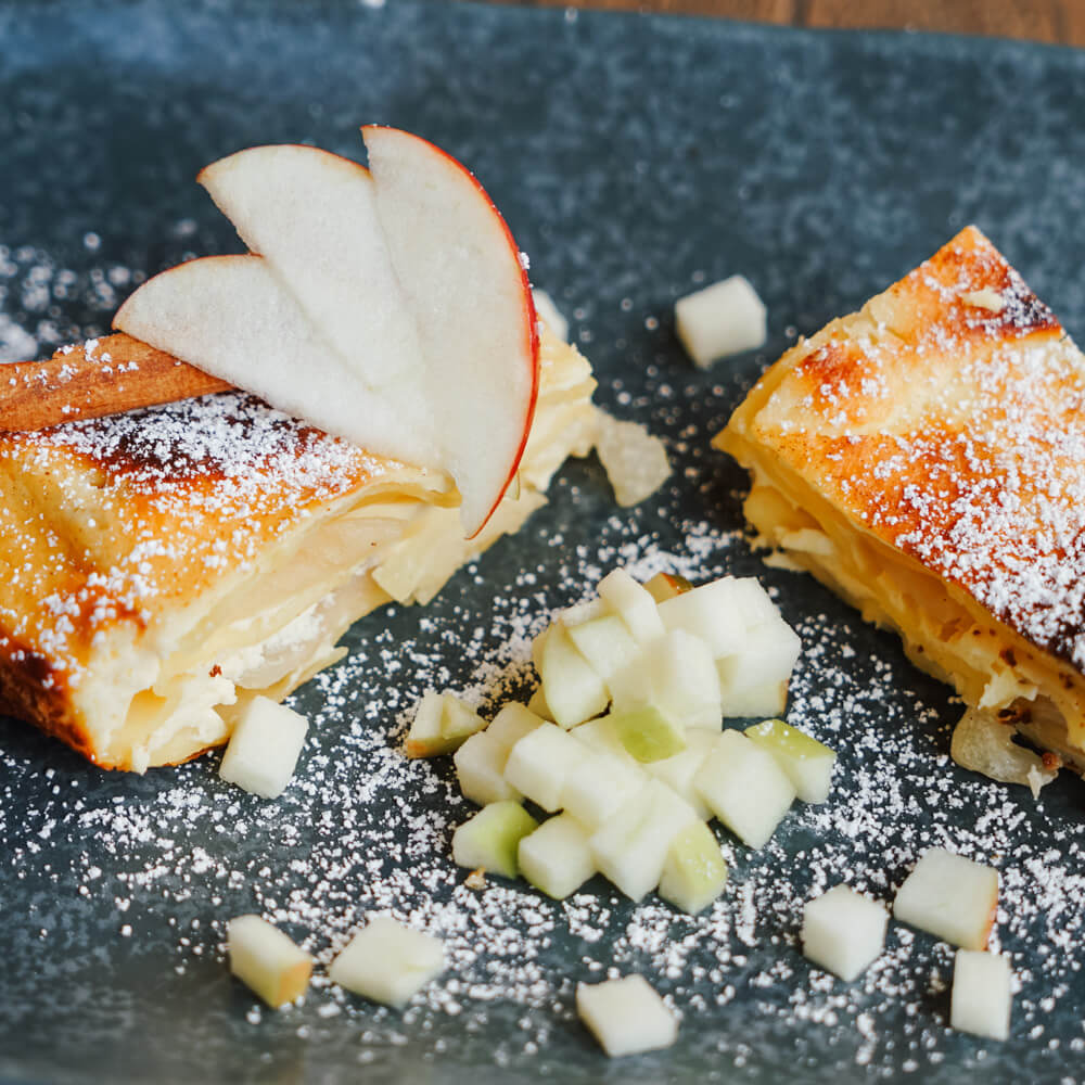 Rezept für Apfellasagne gebackene Apfellasagne mit frischem Apfel und Puderzucker auf dunklem Teller serviert