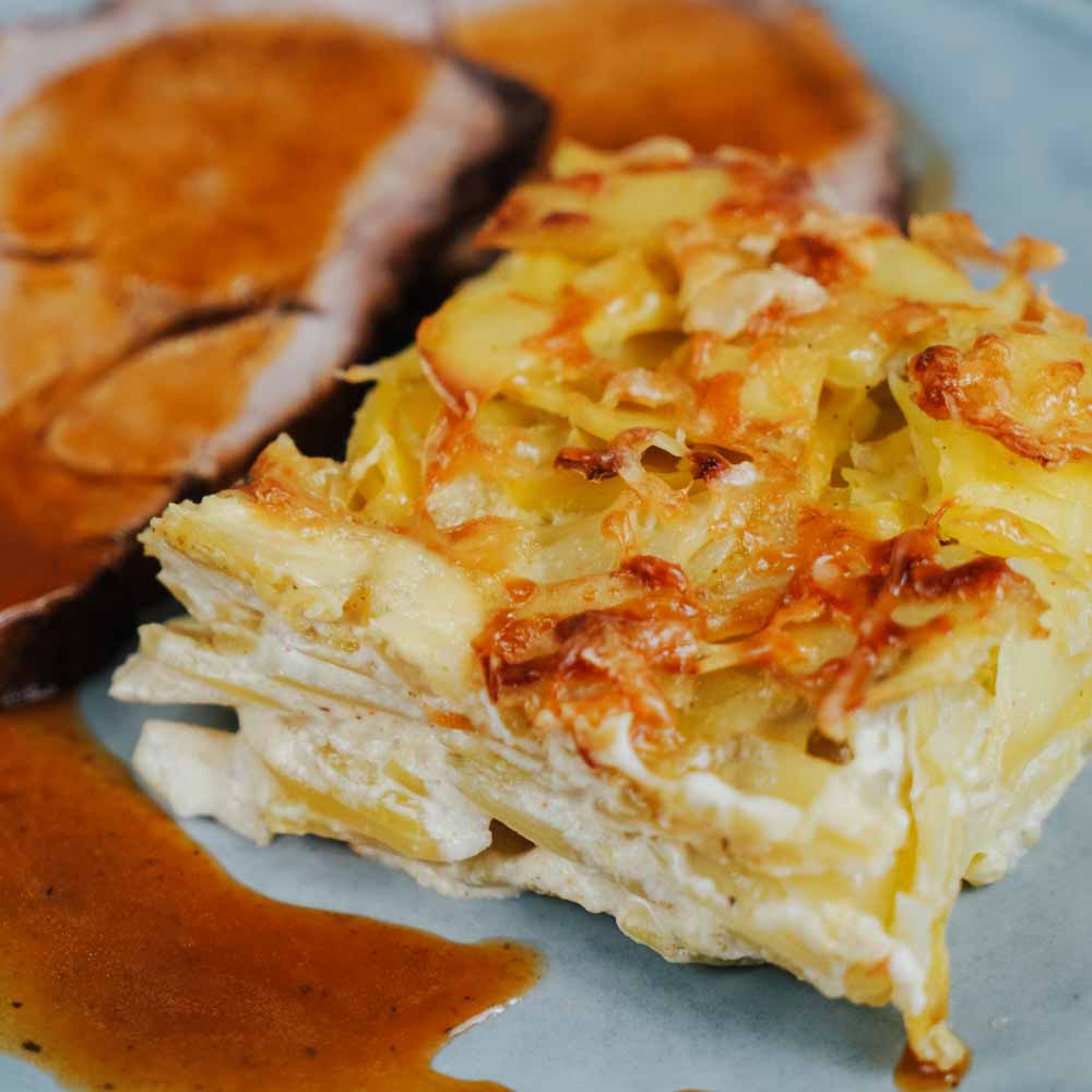 Rezept für Kartoffelgratin cremiges Kartoffelgratin mit Fleisch und Soße auf einem Hellen Teller serviert