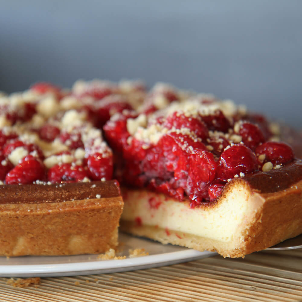 Käsekuchen mit Himbeeren Käsekuchen mit einem Belag aus Himbeeren und Streusel auf einer weißen Kuchenplatte serviert