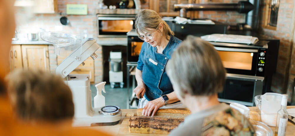 Bäckermeisterin zeigt den Besuchern des Brotfestes bei einer Backvorführung im Backdorf, wie Teig verarbeitet wird - traditionelles Ambiente mit Elektro-Steinbackofen.
